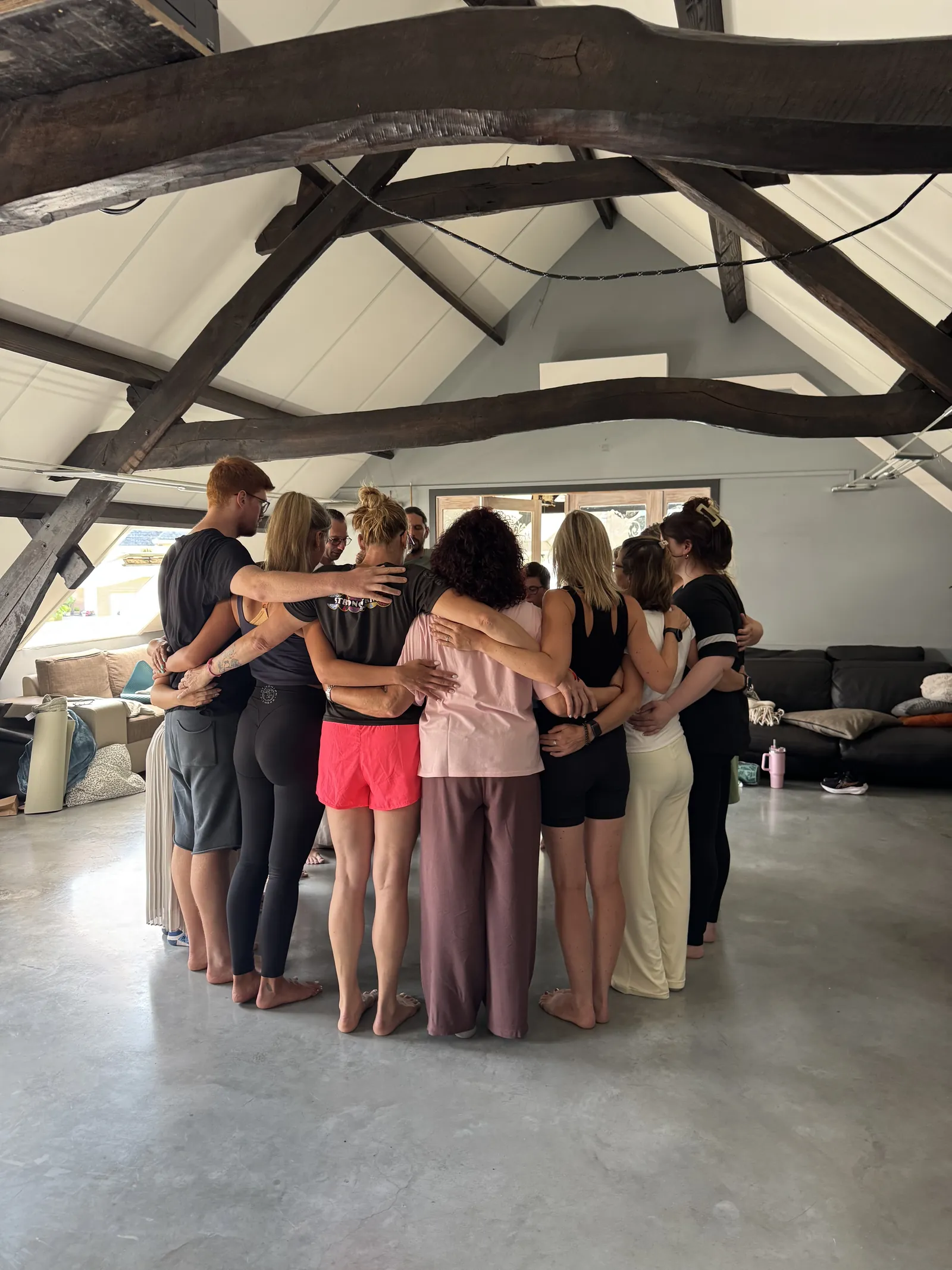 De groep staat in een kring met de armen om elkaar, onder de balken van de retreatruimte.